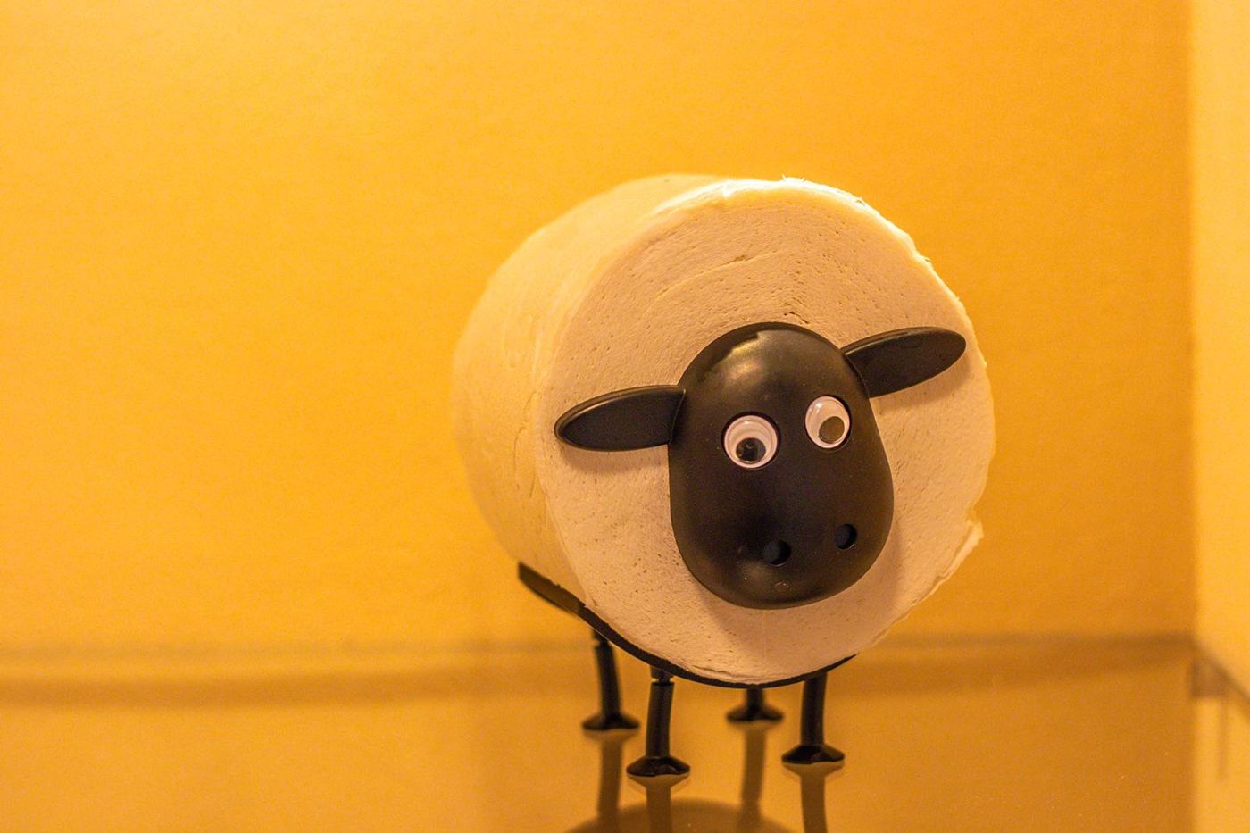 Toiletrolhouder in de vorm van een schaap tegen een okergele wand