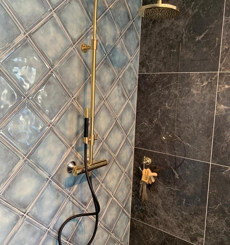 Douchewand met grote tegels in marmerlook en een vak met glasmozaiek