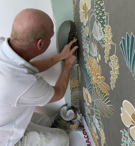Behanger brengt een behang met botanisch dessin naadloos aan op de wand