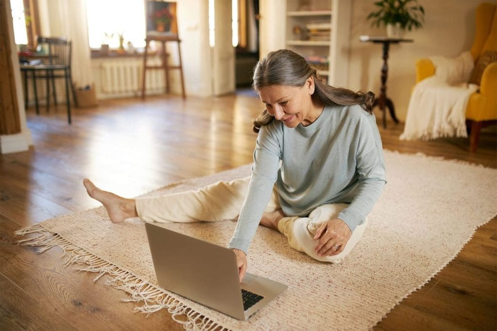 Vrouw zit op de warme vloer in de woonkamer met een laptop